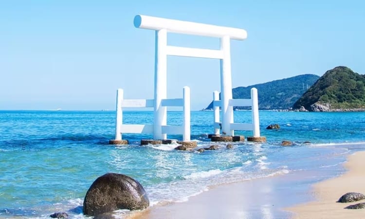 Cổng Torii trắng xóa nổi bật giữa nền trời và nước trong xanh bên bờ biển Futamigaura